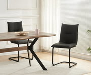 Zwei dunkelgraue Polster-Esszimmerstühle mit schwarzem Metall-Schwinggestell an einem Holzesstisch in hellem Raum, seitliche Perspektive