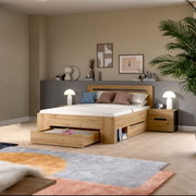 Modernes Holzbett in Eiche-Optik mit gepolstertem Kopfteil, ausziehbarer Bettkasten-Schublade und passendem Nachttisch im Schlafzimmer, fotografiert in frontaler leicht seitlicher Perspektive.