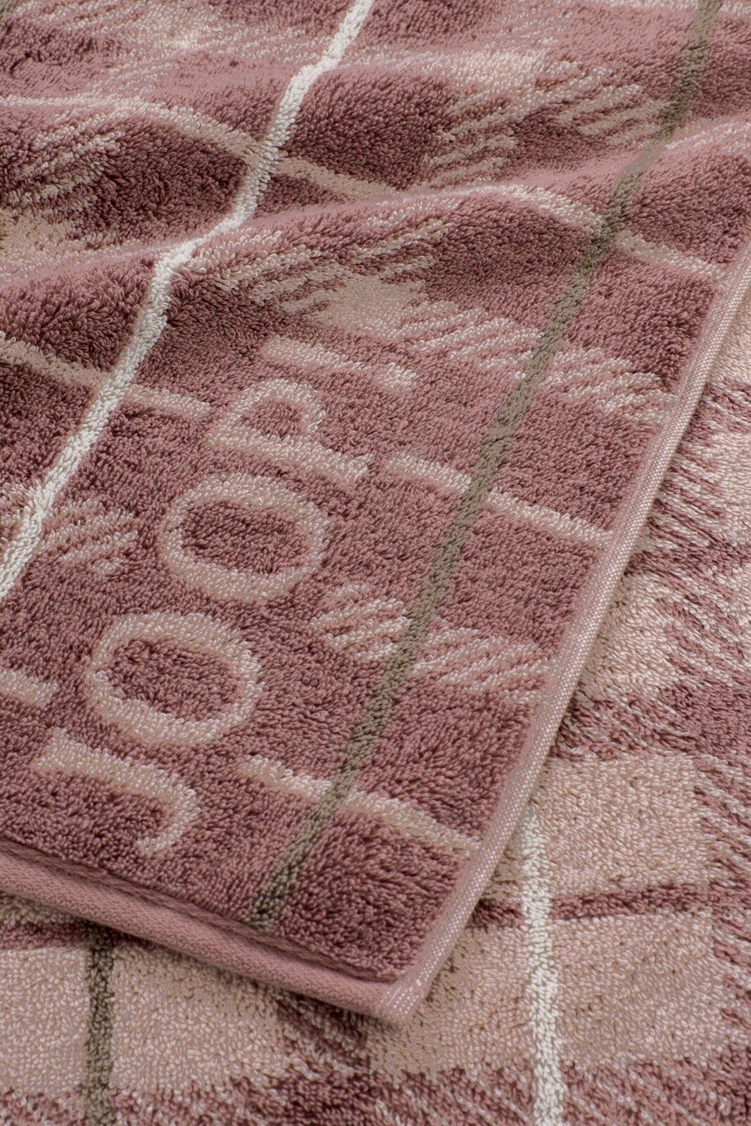 Detailaufnahme eines flauschigen Handtuchs in Altrosa und Beige mit eingewebtem Muster und Bordüre, fotografiert aus schräger Draufsicht