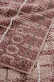Detailaufnahme eines flauschigen Handtuchs in Altrosa und Beige mit eingewebtem Muster und Bordüre, fotografiert aus schräger Draufsicht