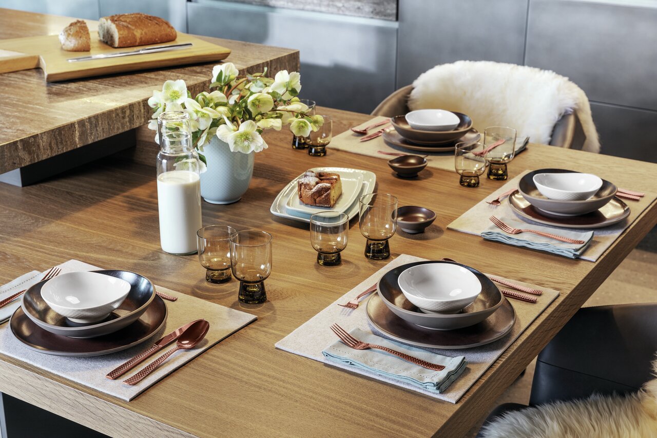 Een elegante tafelsetting met de 30-delige bestekset Cortina in koper op een stijlvol gedekte tafel, gefotografeerd vanuit vogelperspectief.