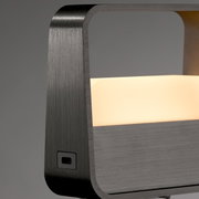 Close-up van een moderne tafellamp met een frame van geborsteld metaal en een verlicht, rechthoekig lichtpaneel.