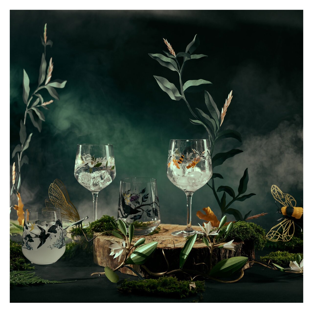 Ritzenhoff Ginglas 2er-Set BOTANIC GLAMOUR Ein Set aus zwei Gingläsern mit kunstvollen Naturmotiven, umgeben von dekorativen Pflanzen und Nebel, aus einer frontalen Perspektive fotografiert.