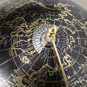 Nahaufnahme eines dekorativen Globus mit schwarzem Hintergrund und goldenen Kontinenten, zeigt die nördliche Hemisphäre mit einem Fokus auf Europa und Russland, mit einem goldenen Meridian und einer Weltzeitskala.