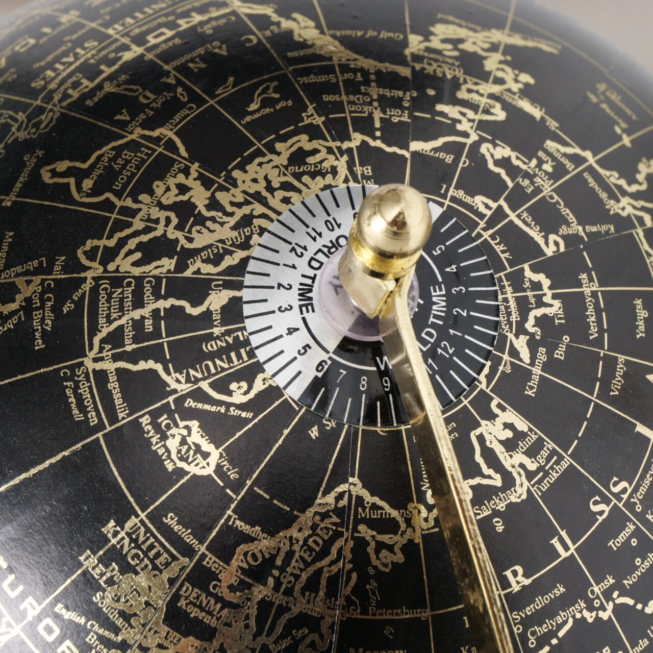Nahaufnahme eines dekorativen Globus mit schwarzem Hintergrund und goldenen Kontinenten, zeigt die nördliche Hemisphäre mit einem Fokus auf Europa und Russland, mit einem goldenen Meridian und einer Weltzeitskala.
