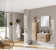 Moderner Badezimmer-Mittelschrank in Holzoptik, links an der Wand montiert, mit dekorativen Elementen und Spiegel im Hintergrund, seitliche Perspektive.
