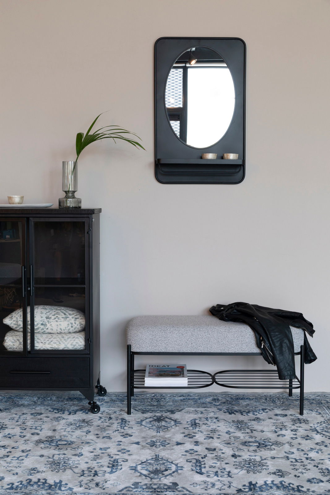 Sitzbank mit grauem Polster und schwarzem Metallgestell, darunter ein Regal mit Zeitschriften, seitliche Perspektive