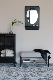 Sitzbank mit grauem Polster und schwarzem Metallgestell, darunter ein Regal mit Zeitschriften, seitliche Perspektive