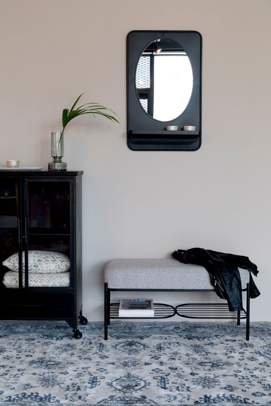 Sitzbank mit grauem Polster und schwarzem Metallgestell, darunter ein Regal mit Zeitschriften, seitliche Perspektive