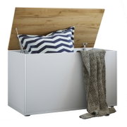 Weiße Aufbewahrungstruhe mit aufgeklapptem Holzdeckel, gefüllt mit Kissen und Decke, in frontaler Perspektive mit leichtem Blick von oben