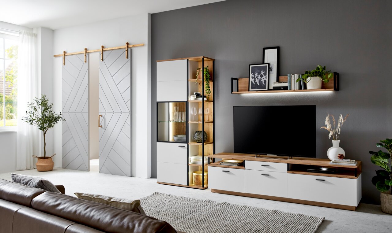 Moderne Wohnzimmer-Wandkombination mit Holz- und Weißakzenten, bestehend aus einem TV-Schrank, einem Regal mit Glasvitrine und einem Wandregal, seitliche Perspektive.