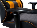 Nahaufnahme eines Gaming-Stuhls mit schwarz-grauer Polsterung und orangefarbenen Akzenten, seitliche Perspektive auf die Armlehne.