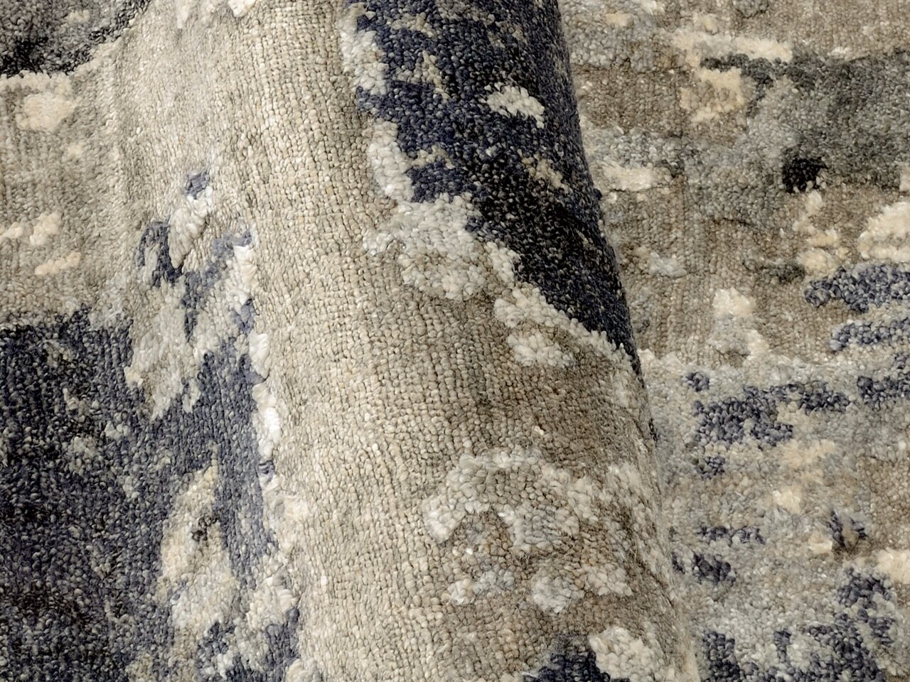 Nahaufnahme eines Designer-Teppichs mit abstraktem Muster in Grau- und Blautönen, perspektivisch von der Seite aufgenommen.