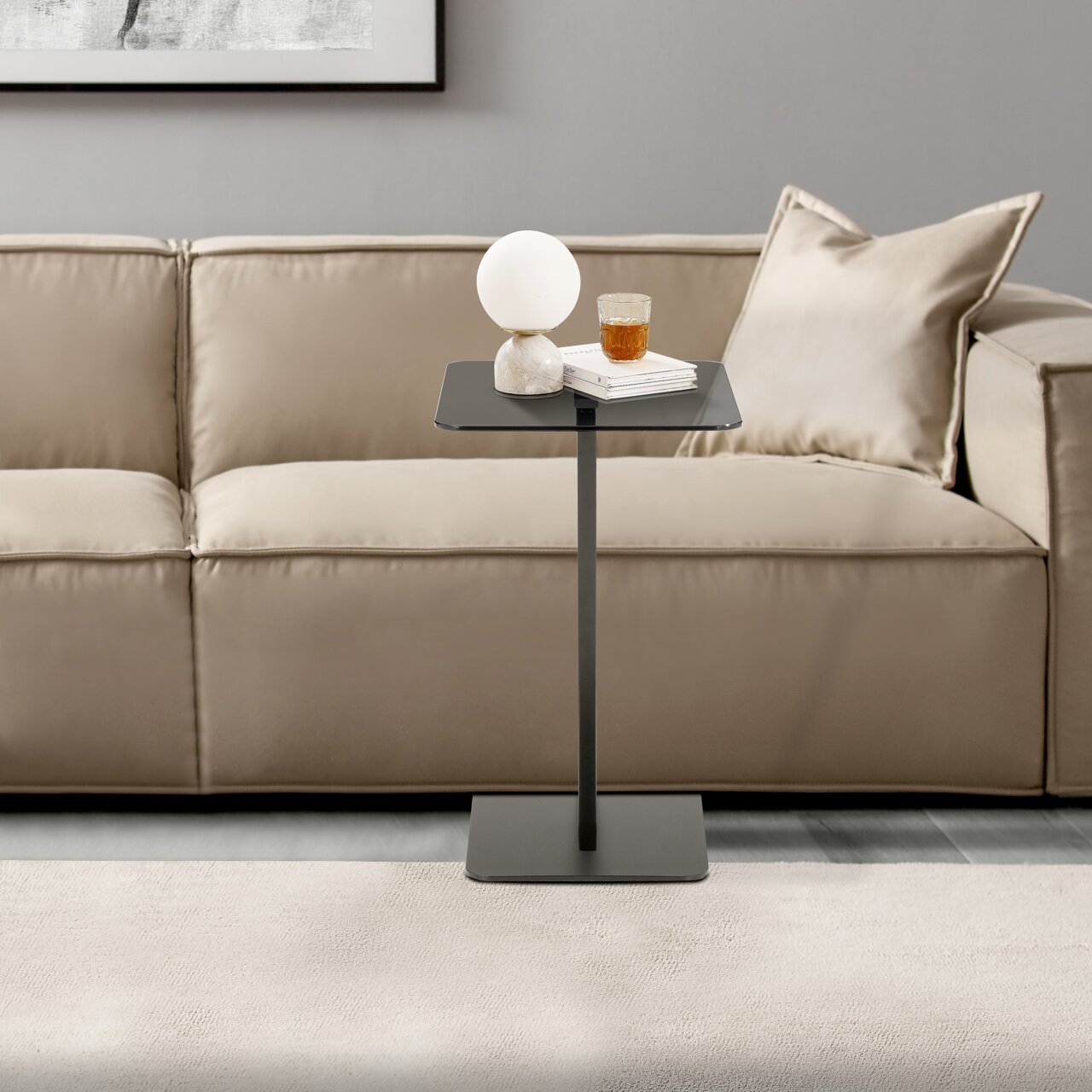 Moderner Beistelltisch in schwarzem Design, frontal vor einem beigen Sofa platziert, mit einer Lampe und einem Glas darauf.