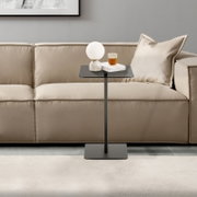 Moderne bijzettafel in een zwart ontwerp, die voor een beige bank staat, met daarop een lamp en een glas.