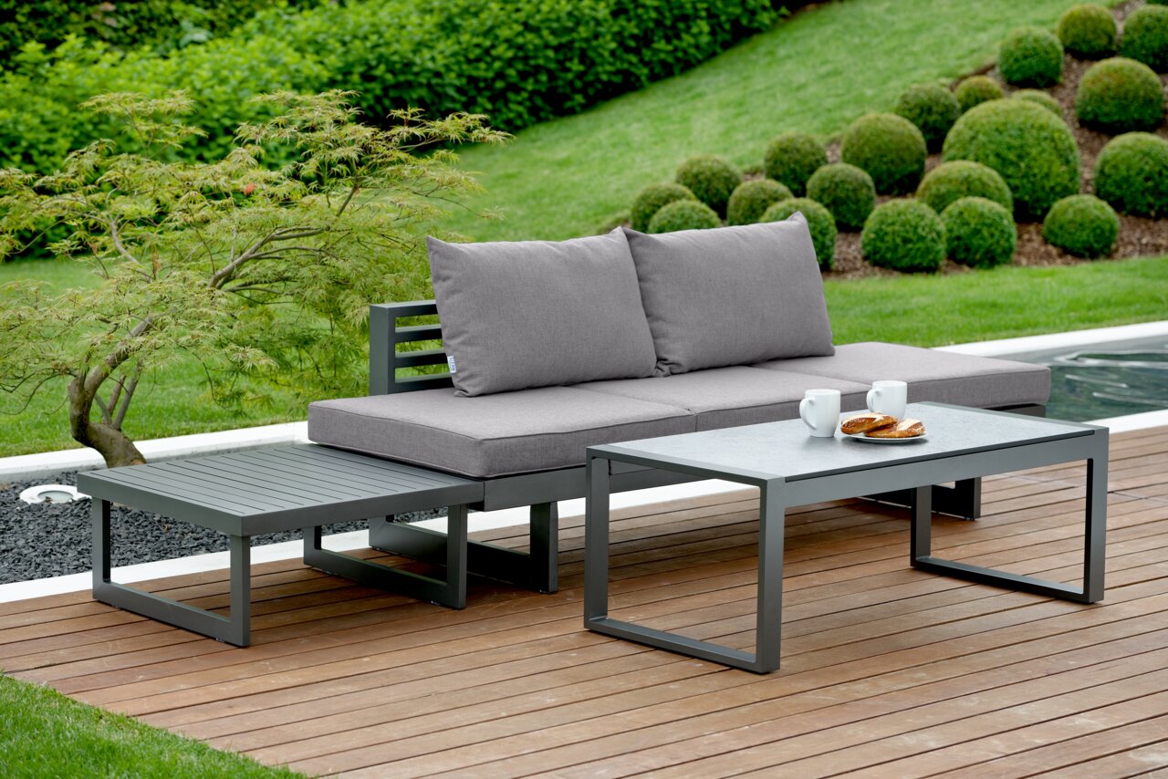 Moderne Lounge-Sitzgruppe im Garten mit grauem Sofa, Couchtisch und Beistelltisch, seitliche Perspektive