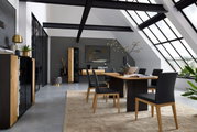 Moderne woonkamerinrichting met eettafel en stoelen in een lichte ruimte met grote ramen, zijaanzicht.