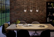 Drie moderne hanglampen boven een eettafel in een stijlvol ingerichte ruimte met een bakstenen muur. Aanzicht van voren.