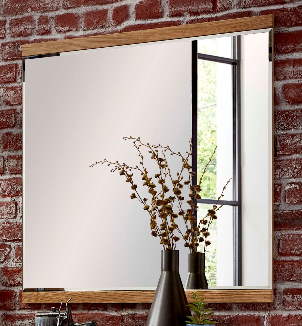 Moderner Wandspiegel mit Holzrahmen, vor einer Ziegelwand, mit Pflanzenvase im Vordergrund, seitliche Perspektive.