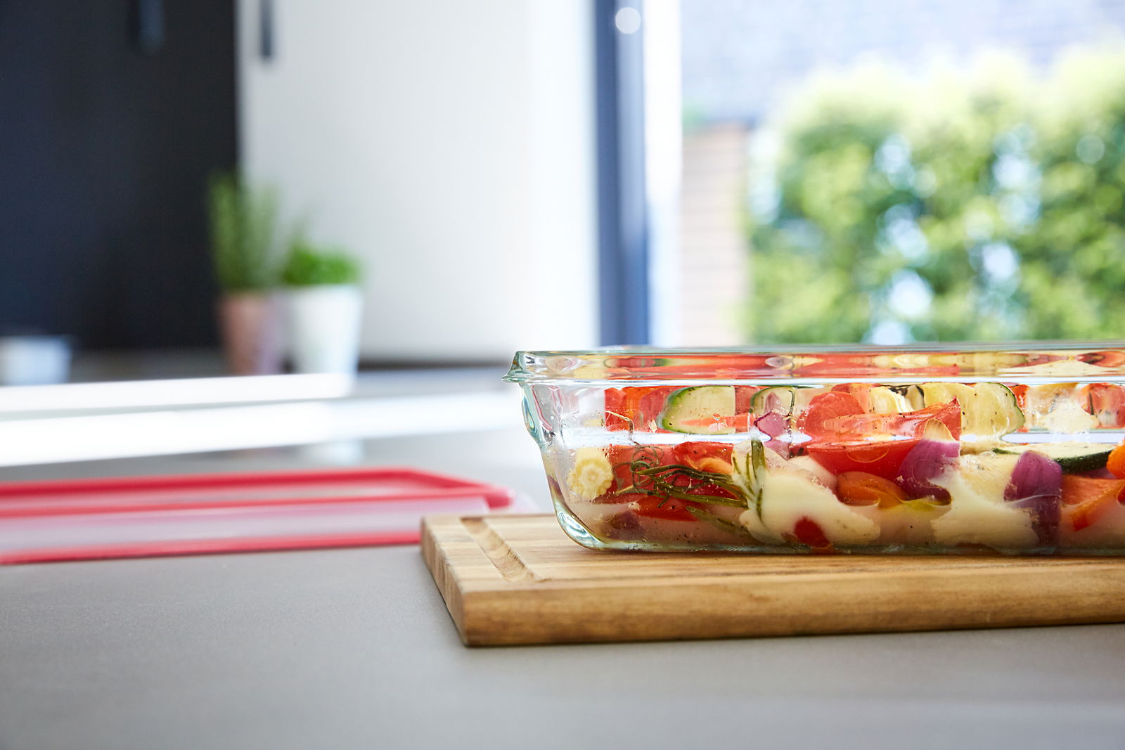 Emsa Frischhaltedose CLIP & CLOSE Rechteckige Glasform mit 0,45 L Fassungsvermögen, gefüllt mit buntem Gemüse, auf einem Holzbrett in einer modernen Küche, seitliche Perspektive.