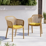 Zwei moderne Outdoor-Stühle aus beigefarbenem Kunststoff mit schlitzförmiger Rückenlehne und gelben Sitzkissen auf heller Terrasse vor weißer Wand und Pflanzen, perspektivisch in leichter Seitenansicht