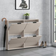 Beiger Schuhschrank mit vier nach vorne klappbaren Fächern und Ablage oben, in frontaler Perspektive leicht von rechts, im Flur mit Pflanze, Schirm und High Heels