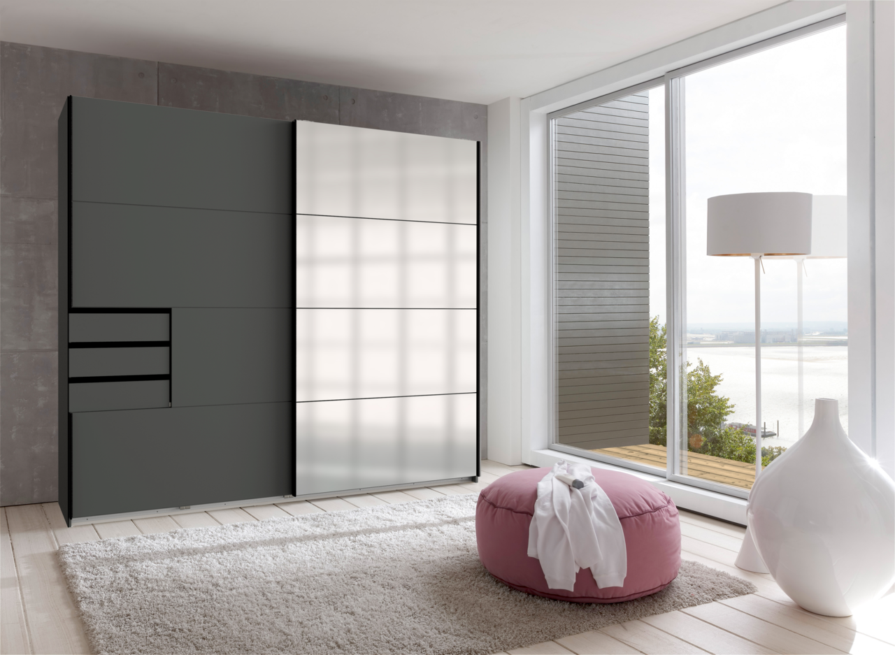 Z2 Schwebetürenschrank 2trg. SAIGON Moderner Schwebetürenschrank mit zwei Türen, links in dunklem Grau und rechts mit spiegelnder Oberfläche, in einem hellen Raum mit Blick auf eine Terrasse.