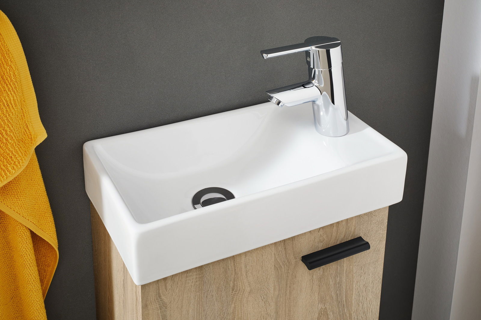 Modernes Waschbecken mit Chromarmatur, Holzunterschrank und gelbem Handtuch, aus der Vogelperspektive fotografiert.