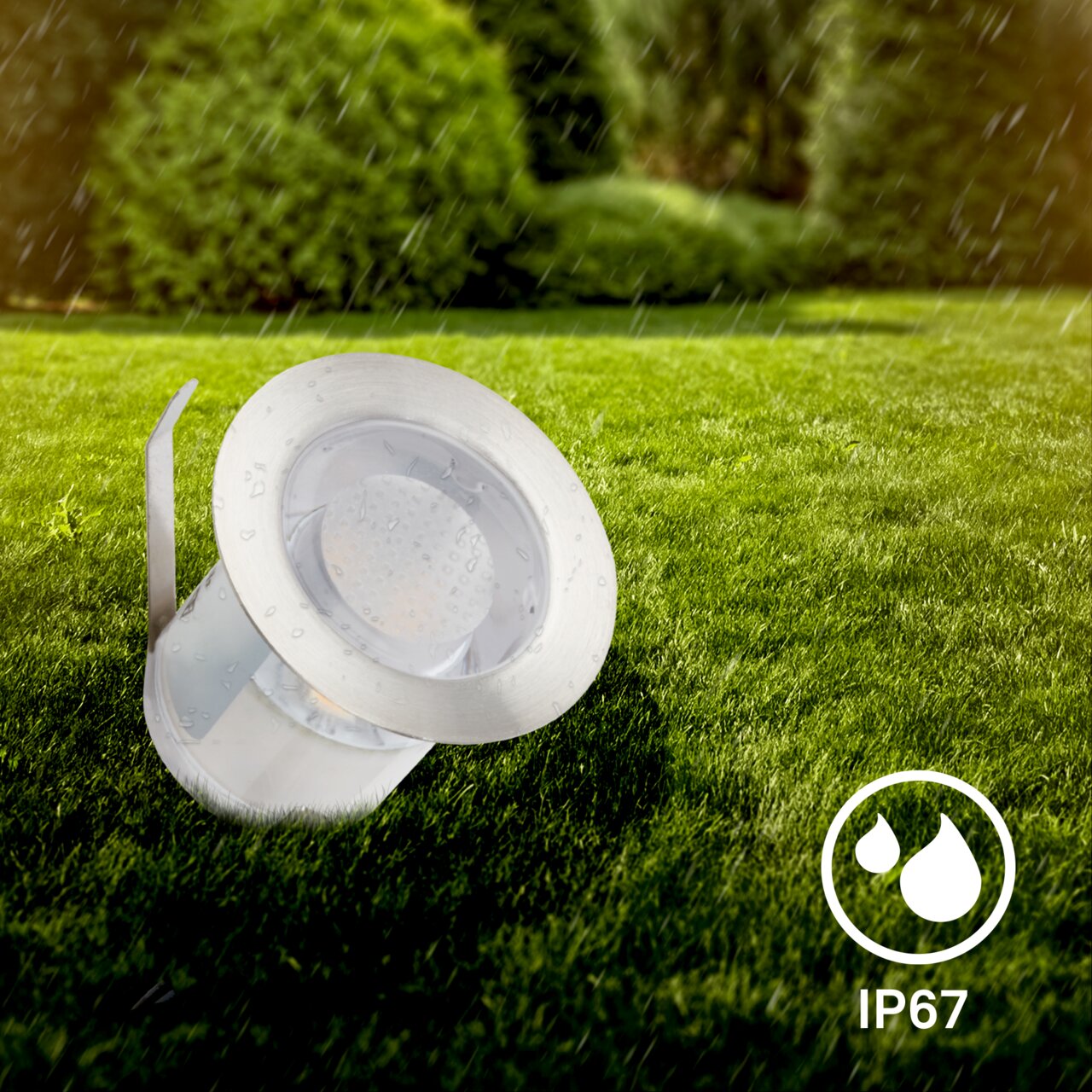 Edelstahl-Bodenleuchte im Regen auf einer Rasenfläche, seitliche Perspektive, IP67-Schutz