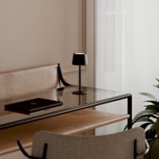 Zwarte, minimalistische tafellamp met een conische kap op een glazen bureau in een moderne werkkamer, zijaanzicht