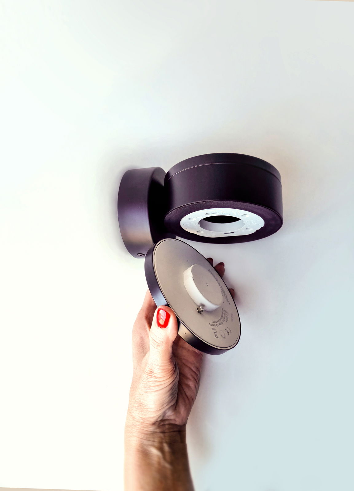 Hand hält eine runde, schwarze LED Wandleuchte aus der Seitenperspektive.