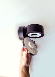 Hand hält eine runde, schwarze LED Wandleuchte aus der Seitenperspektive.