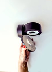 Hand hält eine runde, schwarze LED Wandleuchte aus der Seitenperspektive.