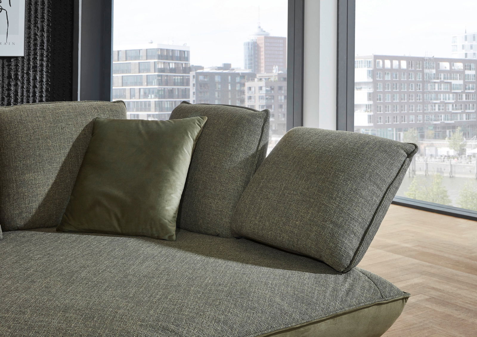 Moderano Longchairkombination ALPHA in Nahaufnahme, zeigt die grüne Polsterung und Kissen, mit Blick aus einem modernen Raum auf die Stadt.