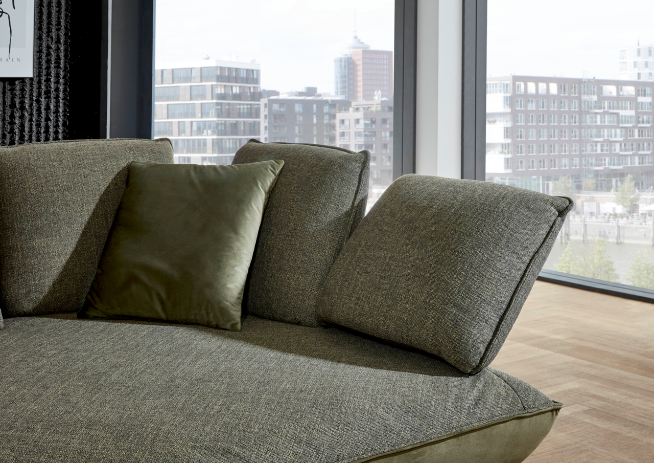 Moderano Longchairkombination ALPHA in Nahaufnahme, zeigt die grüne Polsterung und Kissen, mit Blick aus einem modernen Raum auf die Stadt.