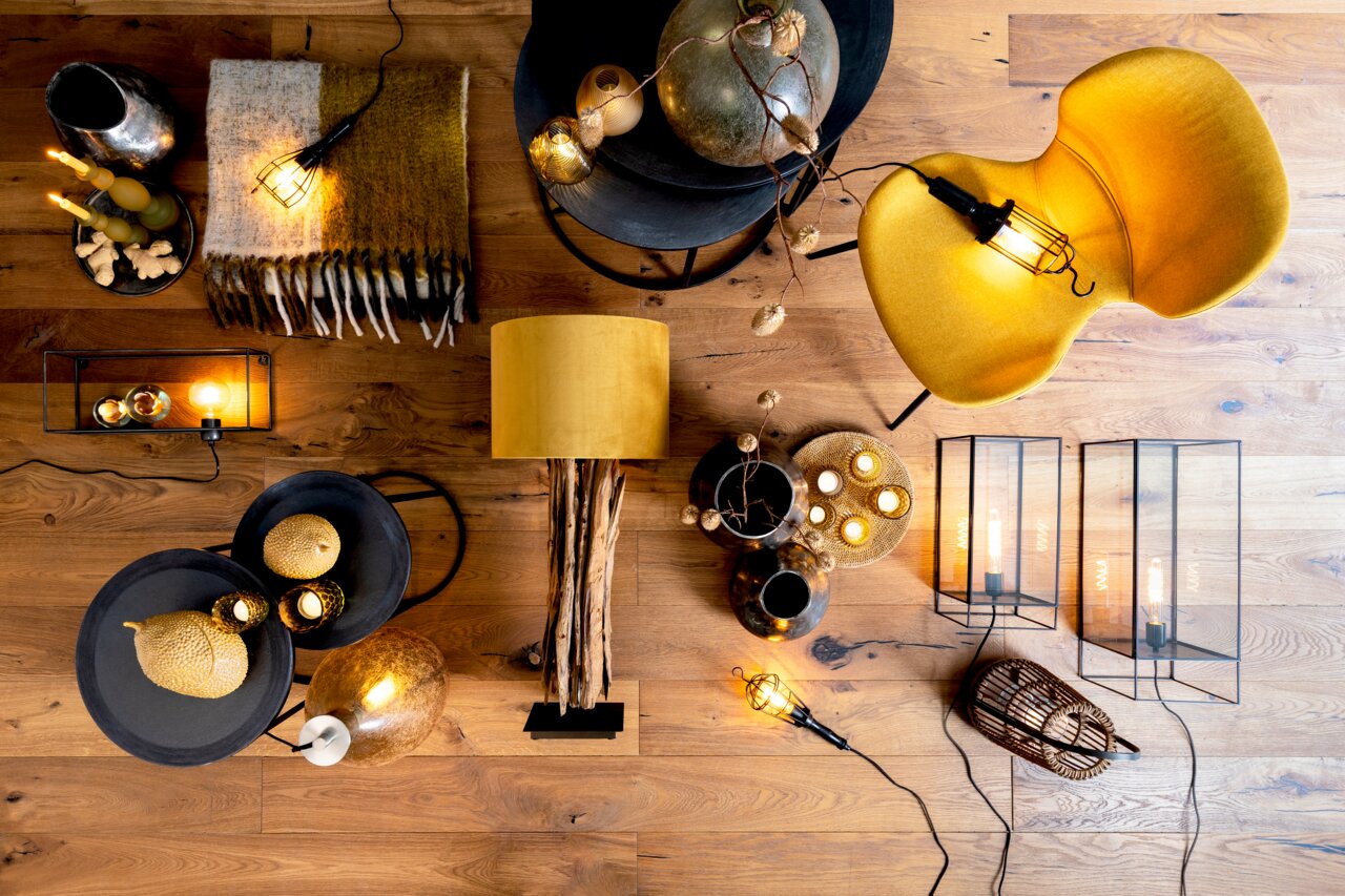 Vogelperspektive auf einen stilvoll dekorierten Raum mit einem Beistelltisch, auf dem goldene Dekorationen und Kerzen stehen, umgeben von einer gelben Lampe, einem gelben Stuhl und weiteren dekorativen Elementen auf einem Holzboden.