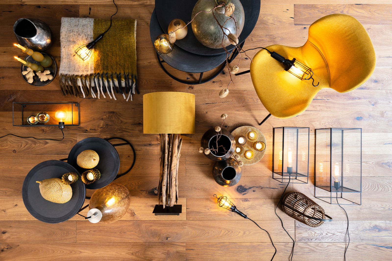 Vogelperspektive auf einen stilvoll dekorierten Raum mit einem Beistelltisch, auf dem goldene Dekorationen und Kerzen stehen, umgeben von einer gelben Lampe, einem gelben Stuhl und weiteren dekorativen Elementen auf einem Holzboden.