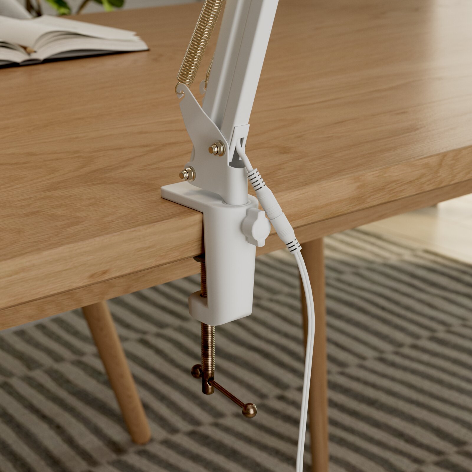 Nahaufnahme in seitlicher Perspektive: weiße Tischklemme einer Schreibtischlampe am Holztisch befestigt, mit Federmechanik und Kabel.