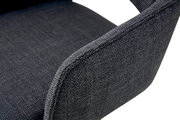 Nahaufnahme eines dunkelgrauen, stoffbezogenen Stuhls mit gepolsterter Rückenlehne und Sitzfläche, schräg von hinten/seitlich fotografiert