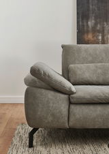 Detailansicht eines grauen Sofas mit verstellbarer Armlehne und Nierenkissen, von der Seite fotografiert.