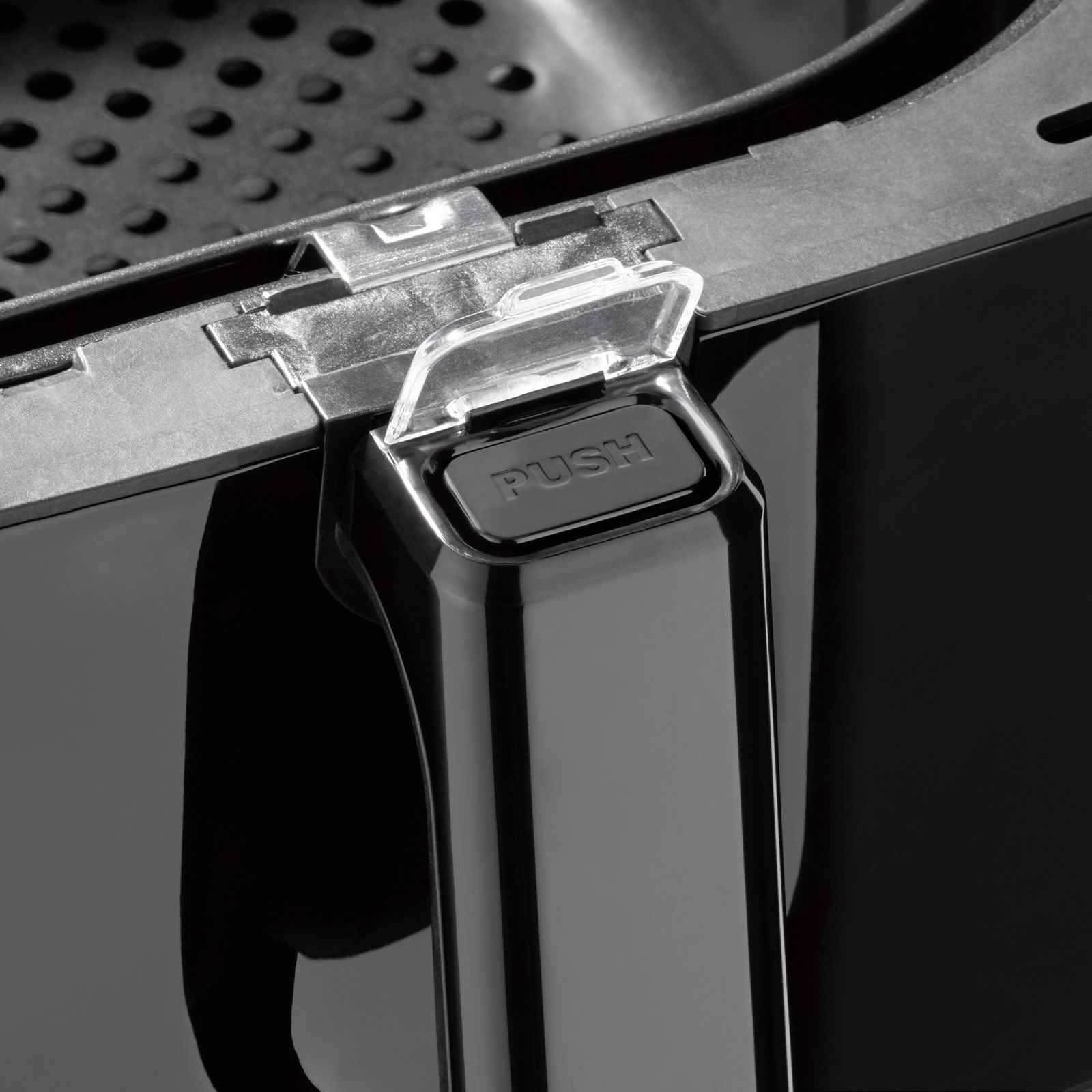 Nahaufnahme eines Griffs einer Heißluftfritteuse mit einem Druckknopf und einem transparenten Verschlussmechanismus.