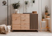 Moderne Kommode aus Holz mit Schubladen und Lamellen-Design, dekoriert mit Pflanzen und Körben, aus frontaler Perspektive.