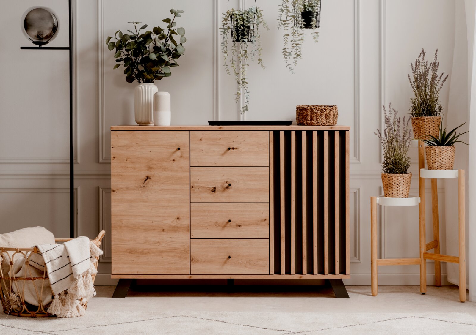 Z2 Ladekast MEDAN Moderne Kommode aus Holz mit Schubladen und Lamellen-Design, dekoriert mit Pflanzen und Körben, aus frontaler Perspektive.