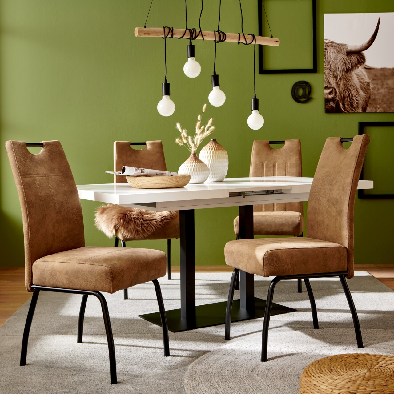 Moderner Esstisch mit weißen Tischplatte und schwarzen Beinen, umgeben von vier braunen Stühlen in einem stilvoll eingerichteten Raum mit grüner Wand. Perspektive: Frontalansicht.