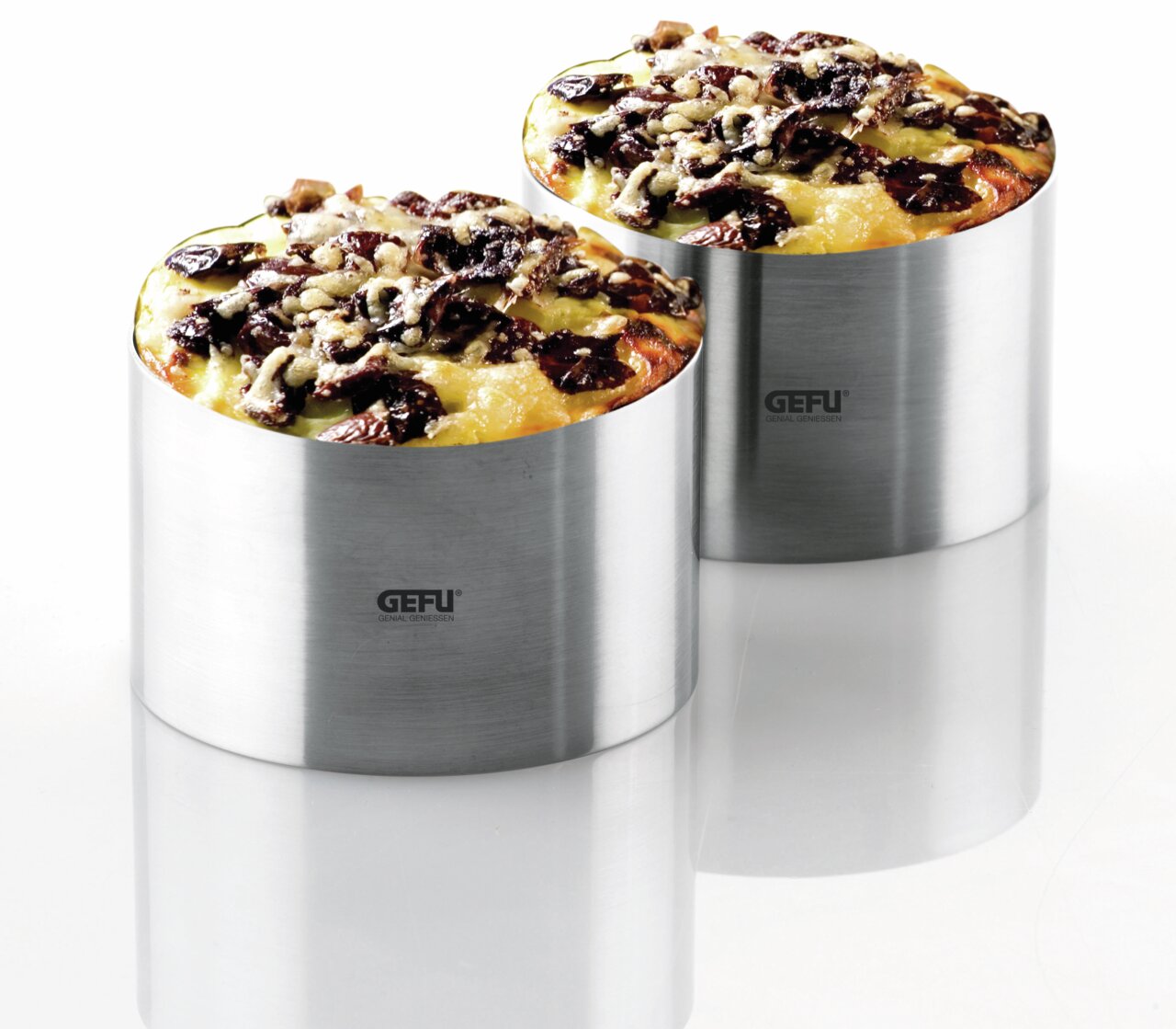 Zwei Edelstahl-Dessert- und Vorspeiseringe mit gefülltem Inhalt, aus seitlicher Perspektive fotografiert.