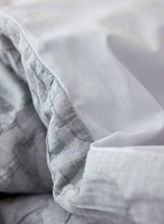 Nahaufnahme von grauer Bettwäsche mit feiner Streifenstruktur und weicher Textur.