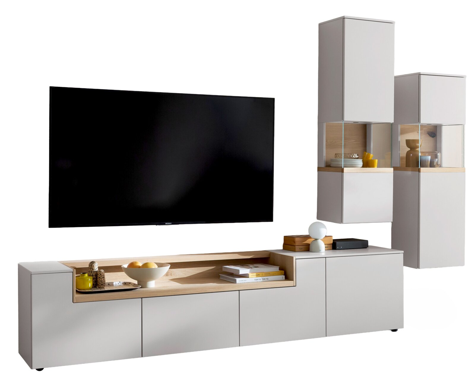 Moderne witte tv-wandmeubelset met eikenhouten accent, laag dressoir en twee vitrinekasten met glas, afgebeeld in schuin vooraanzicht met een grote flatscreen tv