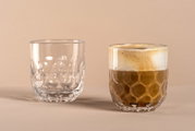 Zwei Gläser mit 220ml Volumen, eines leer und eines mit Kaffee gefüllt, auf einer neutralen Oberfläche. Die Gläser haben ein einzigartiges, tropfenförmiges Design. Perspektive von vorne.