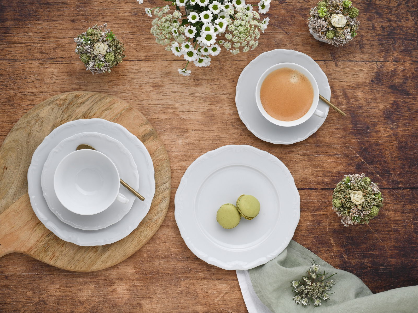 Kaffeeservice 18-tlg aus der Vogelperspektive auf einem Holztisch arrangiert, mit Tassen, Untertassen, Tellern und goldenen Löffeln, umgeben von Blumen und Gebäck.