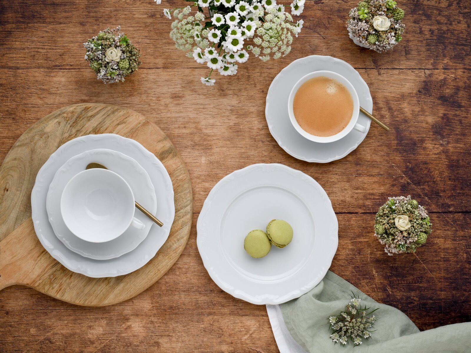 Kaffeeservice 18-tlg aus der Vogelperspektive auf einem Holztisch arrangiert, mit Tassen, Untertassen, Tellern und goldenen Löffeln, umgeben von Blumen und Gebäck.